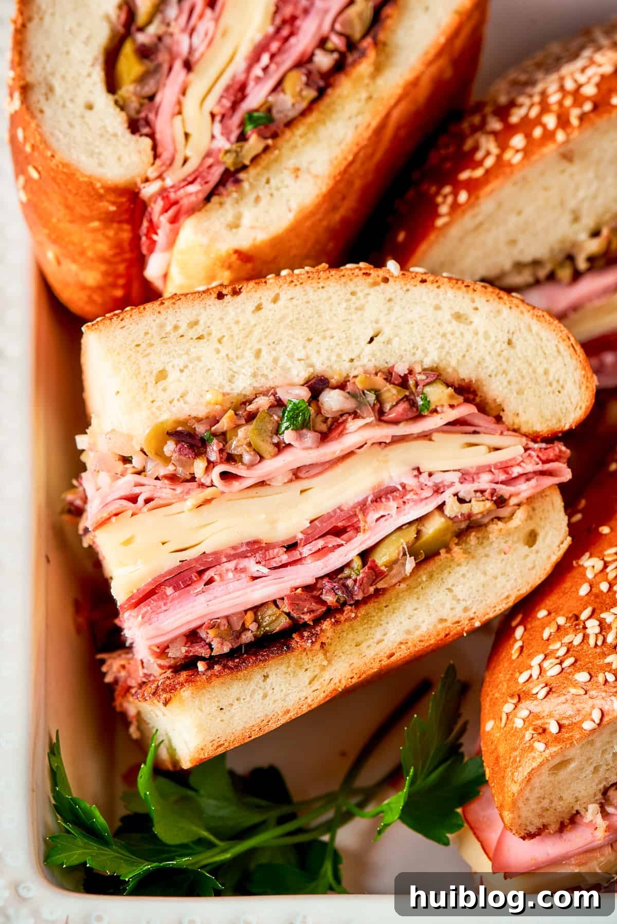 A freshly made Muffaletta sandwich, sliced in half to reveal generous layers of meat, cheese, and olive salad, sits on a wooden cutting board.