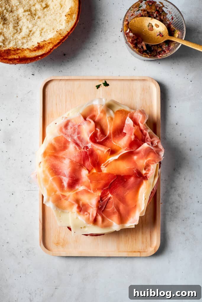 Delicate slices of prosciutto are gently placed over the cheese and other meats, enhancing the sandwich's gourmet appeal.