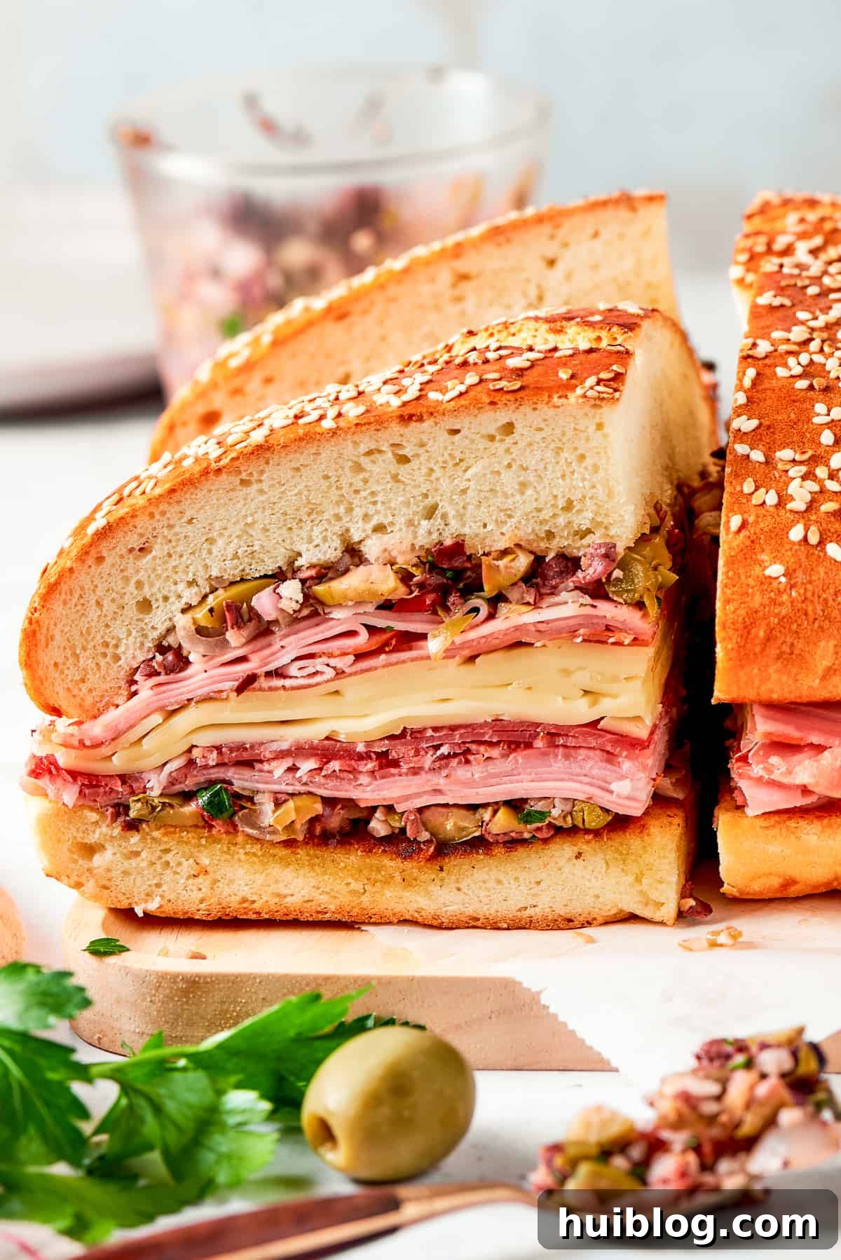 Two generous pieces of a tall muffaletta sandwich, showcasing its many layers, presented on a cutting board, ready to be enjoyed.
