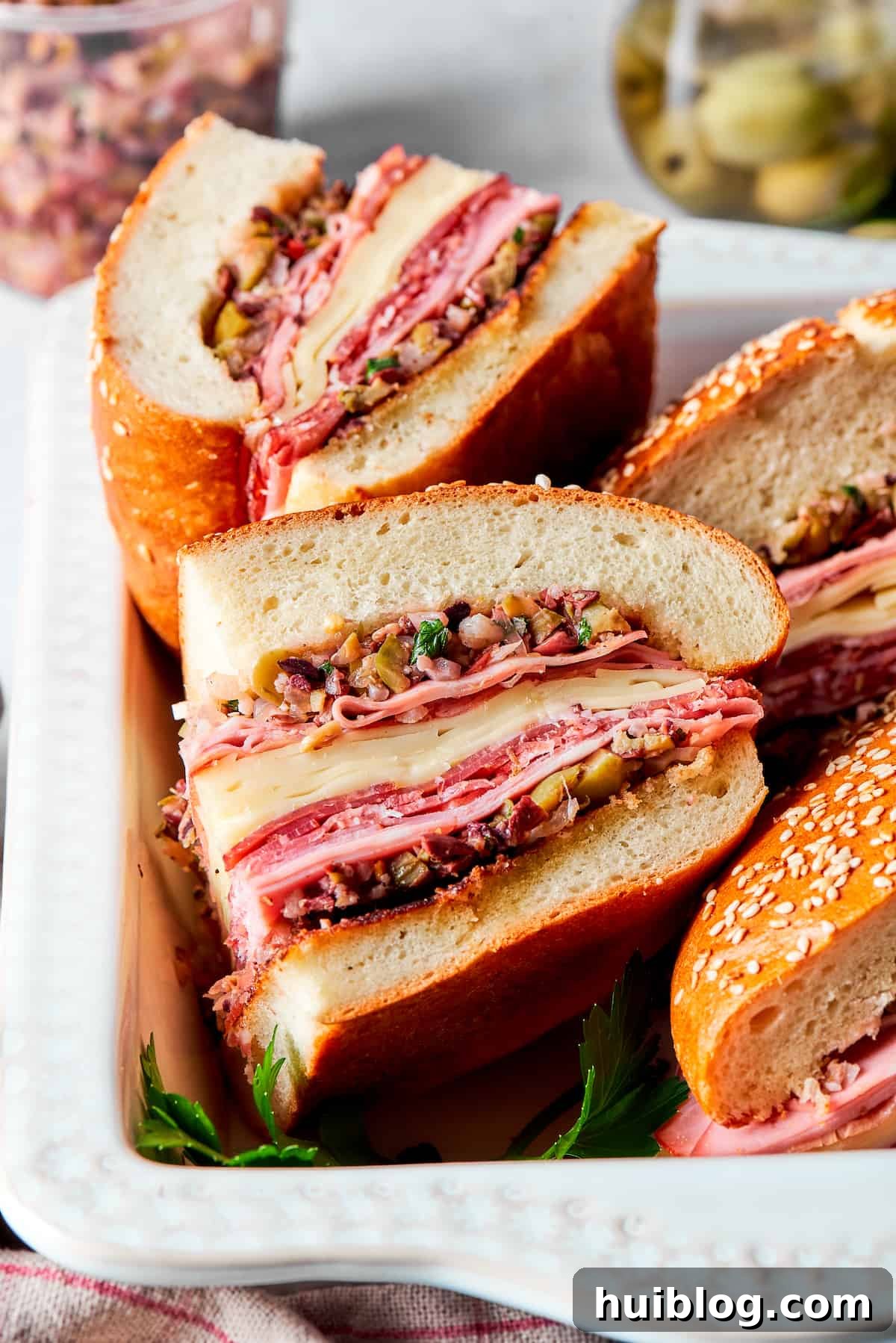 Two vibrant, layered pieces of muffaletta sandwich, showcasing the generous meat, cheese, and olive salad fillings, ready for enjoyment.