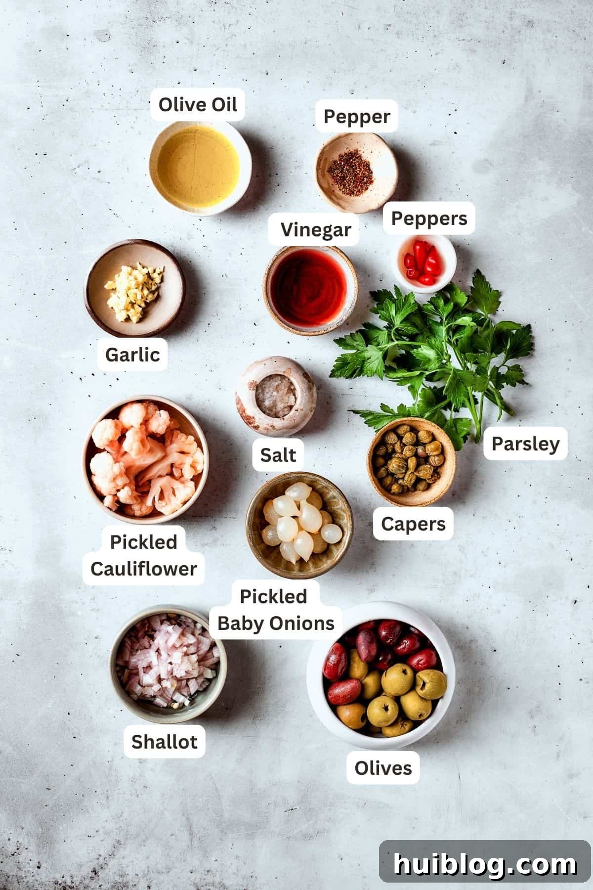 A vibrant display of fresh ingredients for olive salad including green and black olives, capers, peppers, pickled cauliflower, garlic, and herbs.