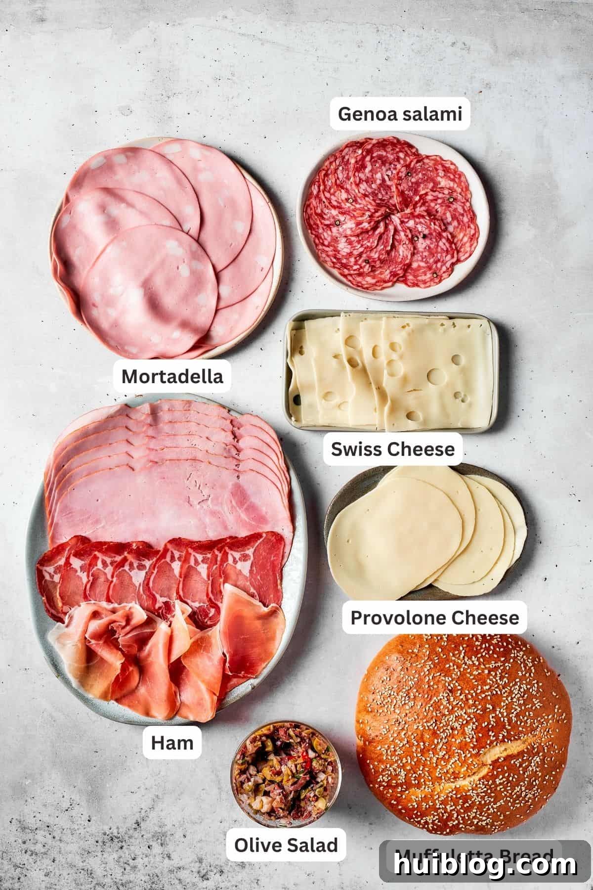 An array of thinly sliced deli meats and cheeses, including mortadella, salami, ham, prosciutto, Swiss, and Provolone cheese, alongside olive salad.
