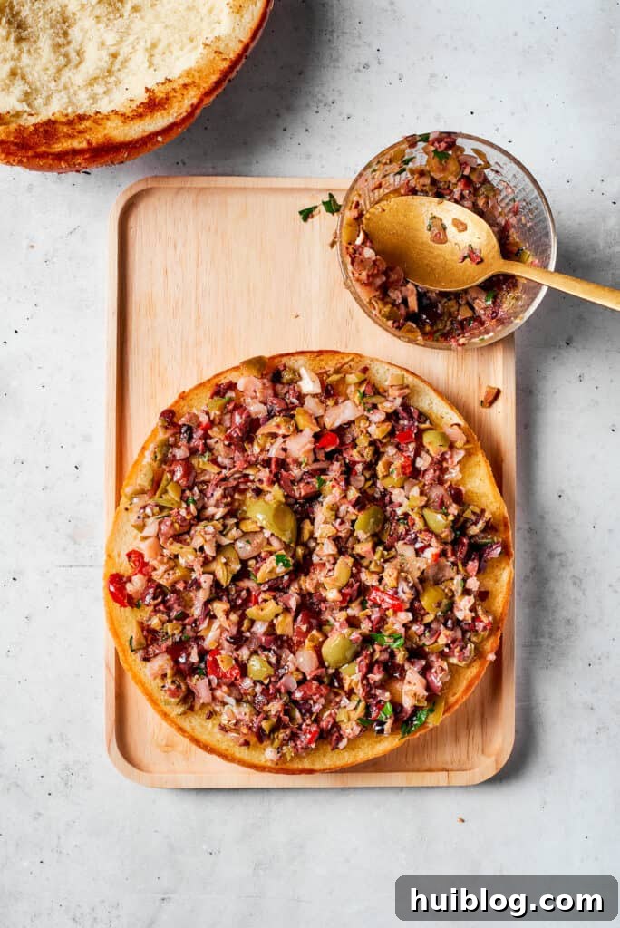A generous layer of homemade olive salad is spread evenly over one half of the toasted bread.