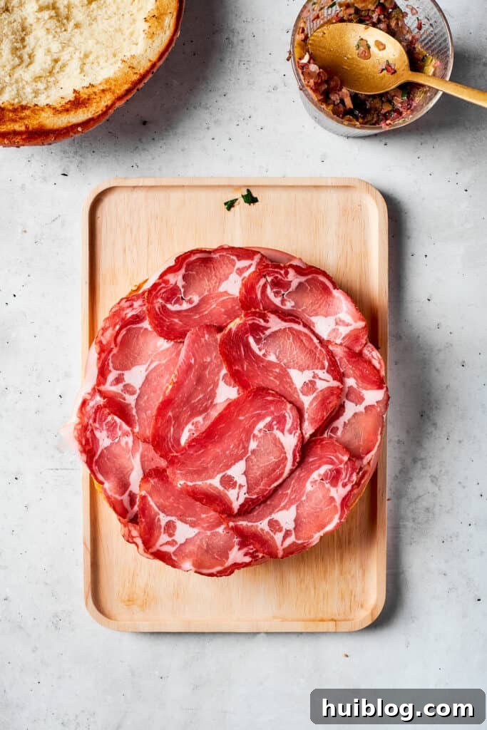 Thinly sliced deli ham is carefully arranged to cover the previous layers of meat.
