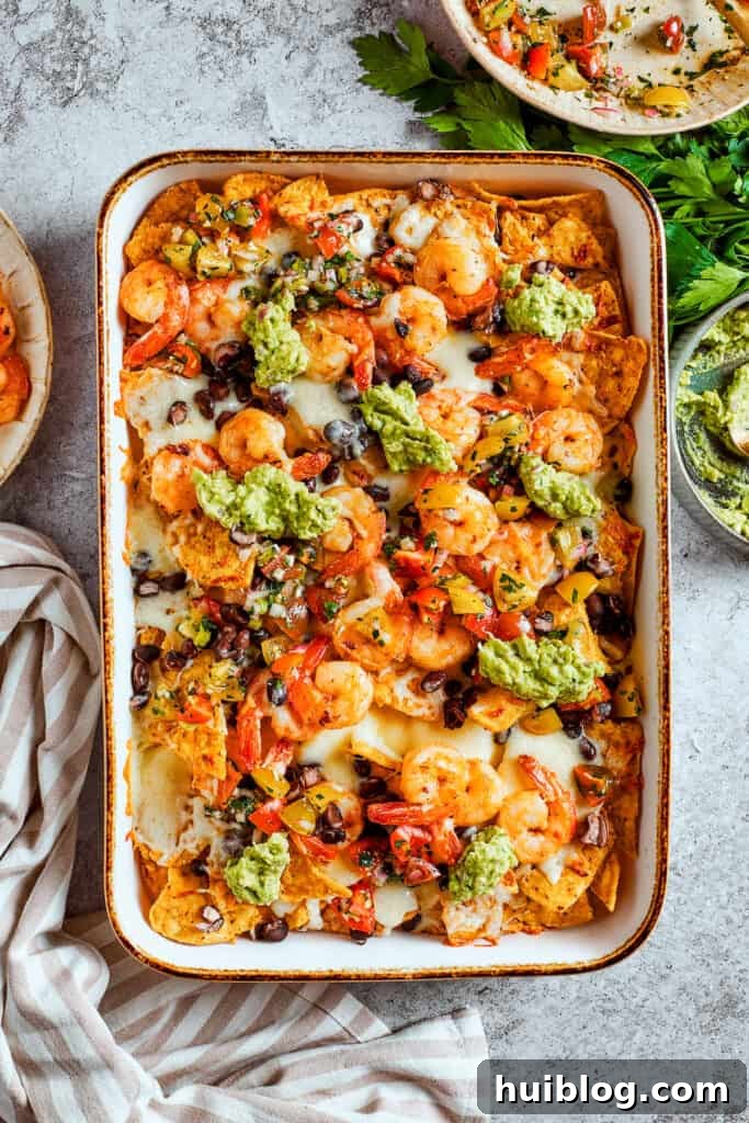Coastal Crunch Shrimp Nachos 11 Guacamole is dolloped onto the tray of shrimp nachos.