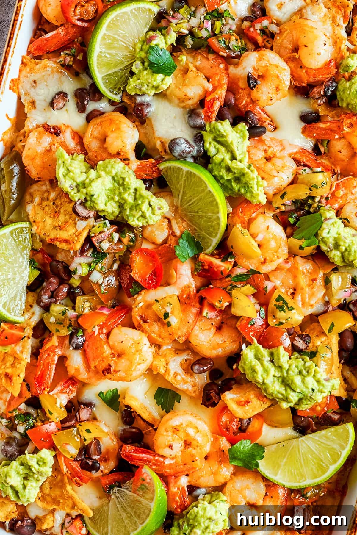 Coastal Crunch Shrimp Nachos 12 Tortilla chips topped with shrimp, cheese, black beans, tomatoes, and a garnish of guacamole and slices of lime.