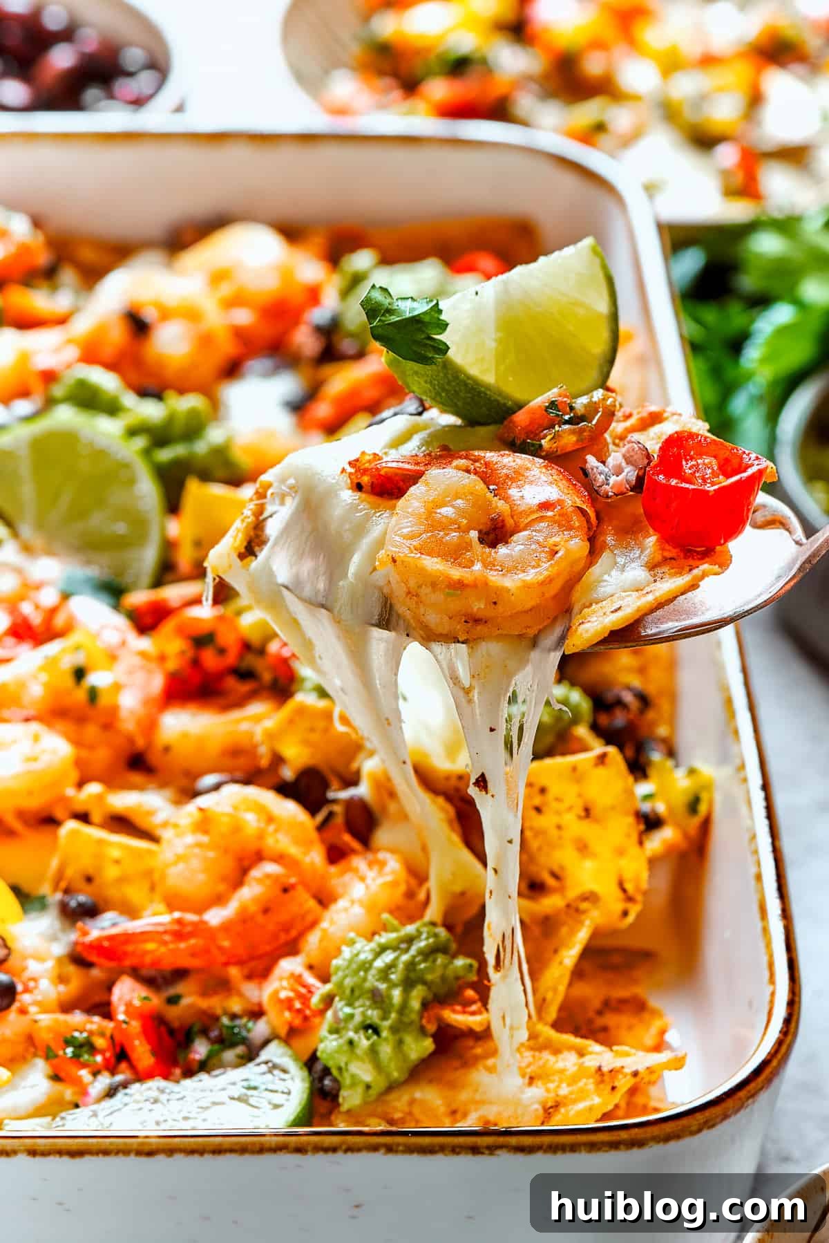Coastal Crunch Shrimp Nachos 13 A spoon lifts out a cheesy portion of shrimp nachos.