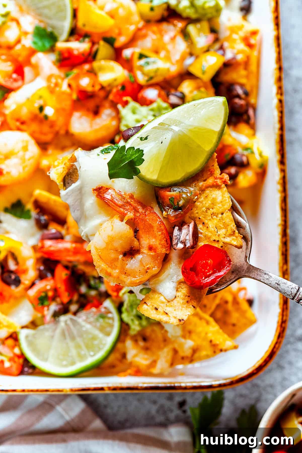 Coastal Crunch Shrimp Nachos 5 A spoon lifts out nachos from a baking dish.