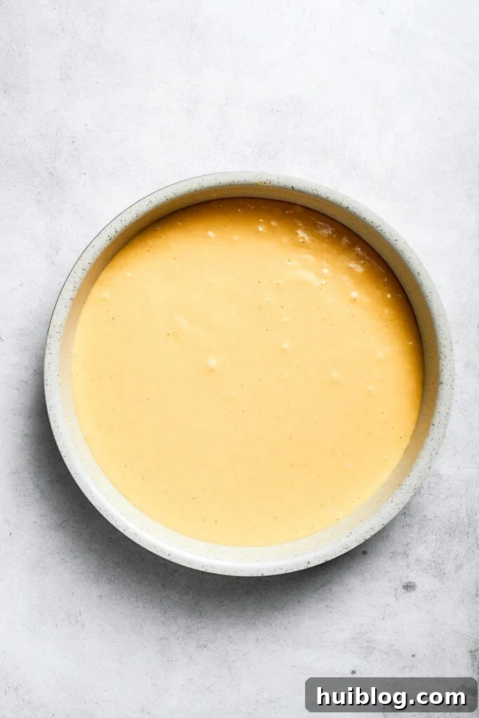 The prepared cake batter is being poured over the pineapple and cherry layer in the cake pan, ready for baking.