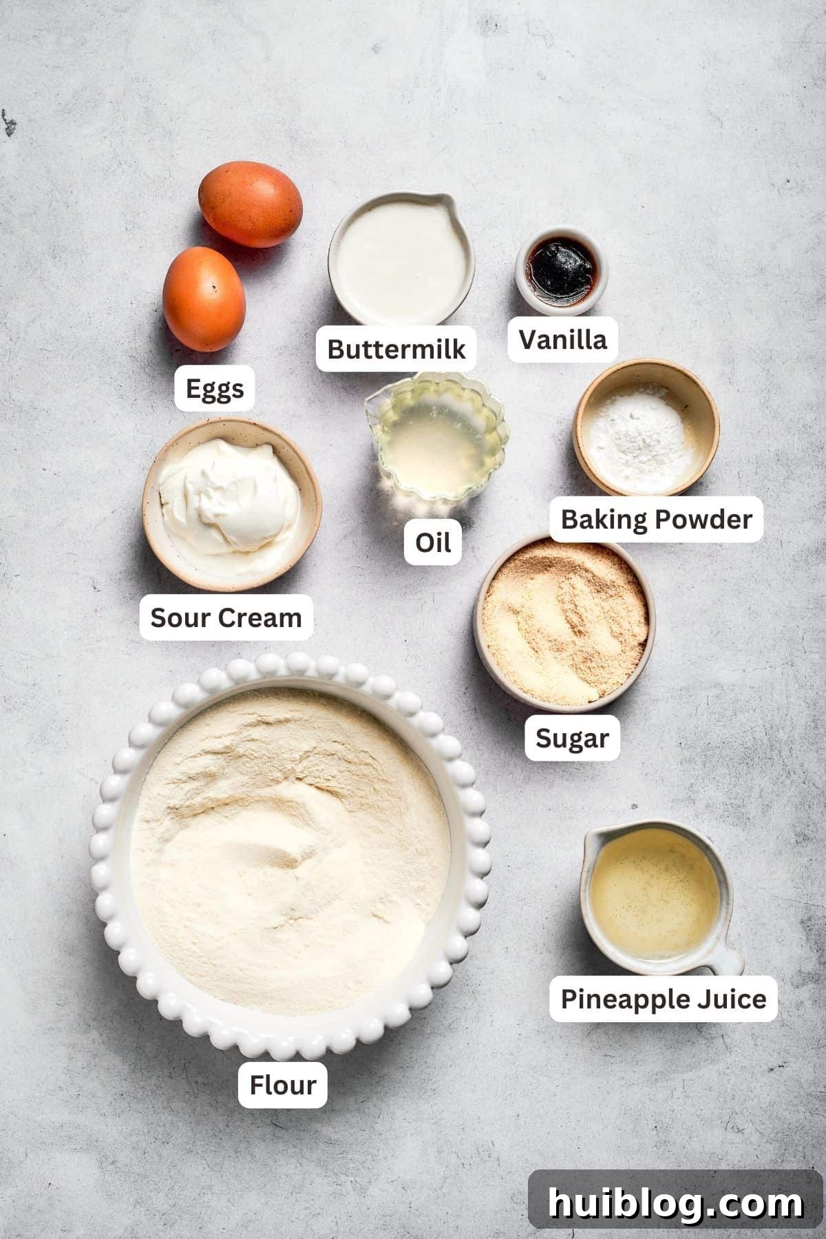 Cake batter ingredients displayed: all-purpose flour, reserved pineapple juice, baking powder, granulated sugar, vegetable oil, pure vanilla extract, buttermilk, sour cream, and large eggs.