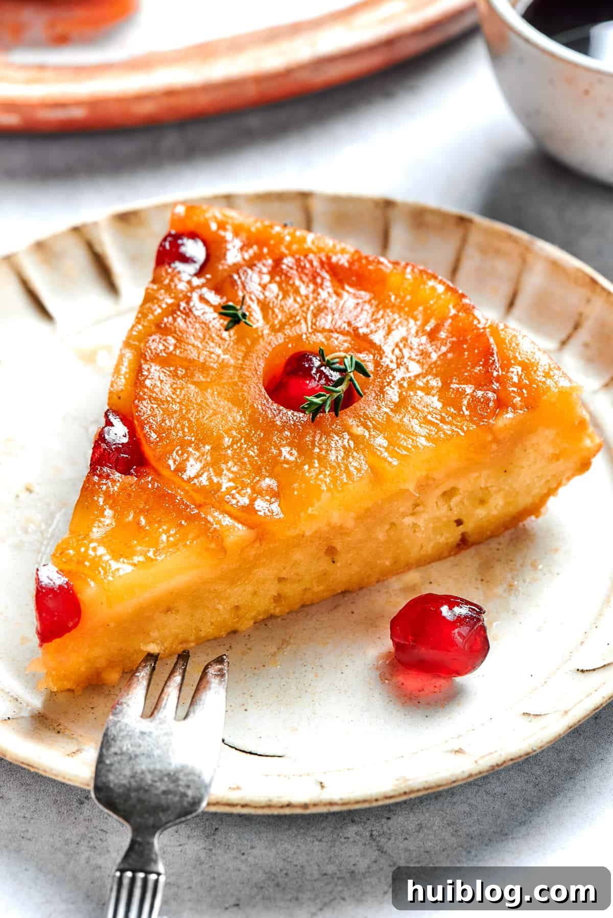 A perfectly baked slice of pineapple upside-down cake, revealing the golden pineapple and cherry topping, served on a white plate with a fork.