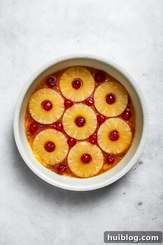 Juicy pineapple rings are carefully arranged over the butter and brown sugar mixture, with bright red maraschino cherries placed in their centers.