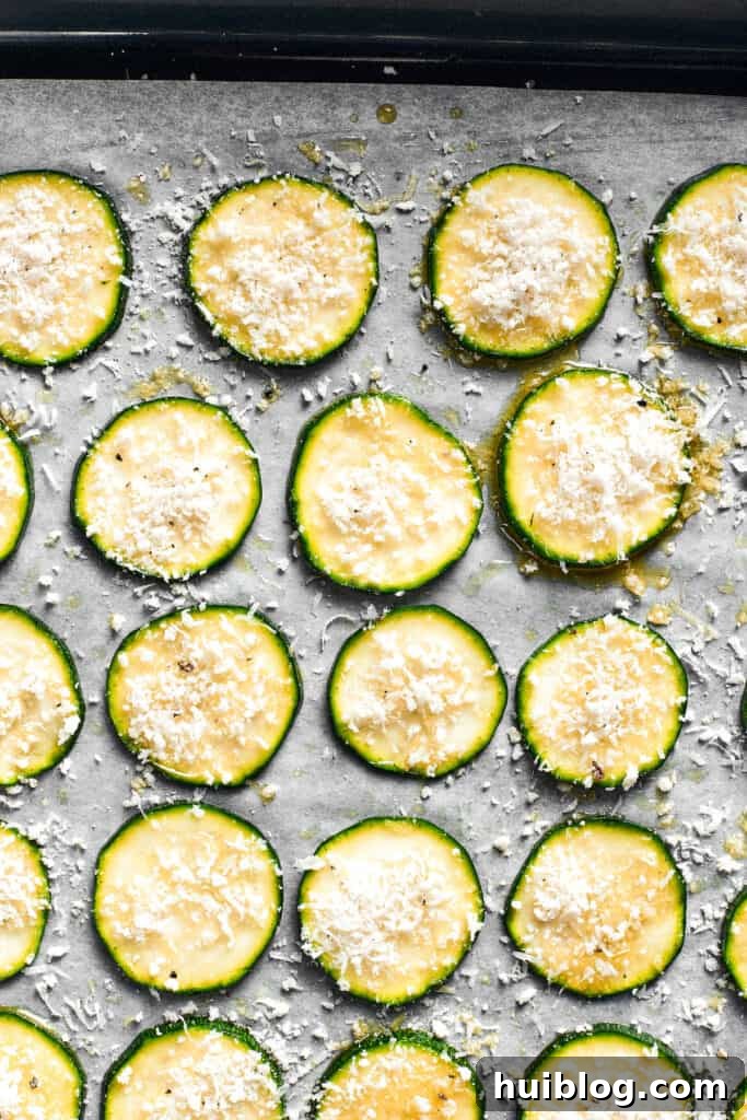 The zucchini chips are neatly spread out on a lined baking sheet, coated with breadcrumbs.
