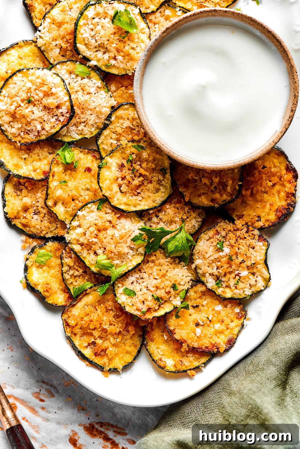 A generous platter of freshly baked, golden-brown zucchini chips, garnished with fresh greenery, ready for serving.