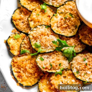 A pile of golden-brown zucchini chips arranged neatly on a white plate, garnished with fresh herbs.