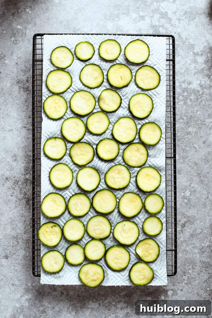 A large baking sheet covered with a single layer of thinly sliced zucchini rounds, salted and draining.