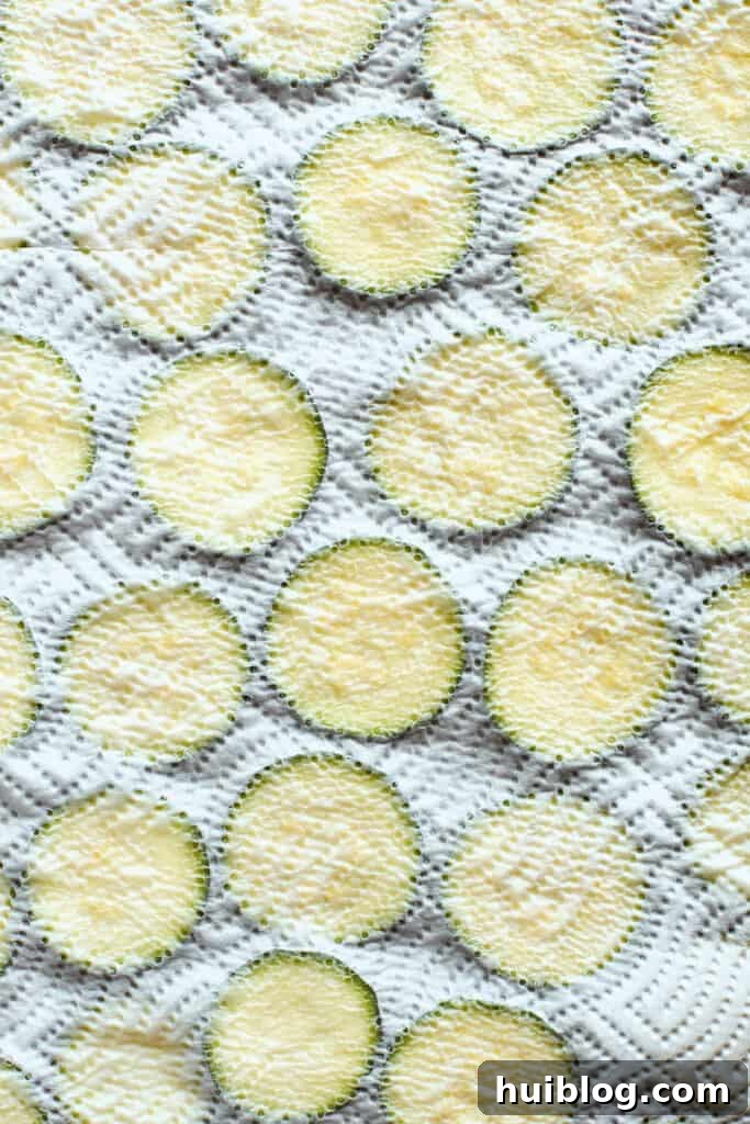 A paper towel delicately covering a baking sheet of zucchini slices, absorbing excess moisture.