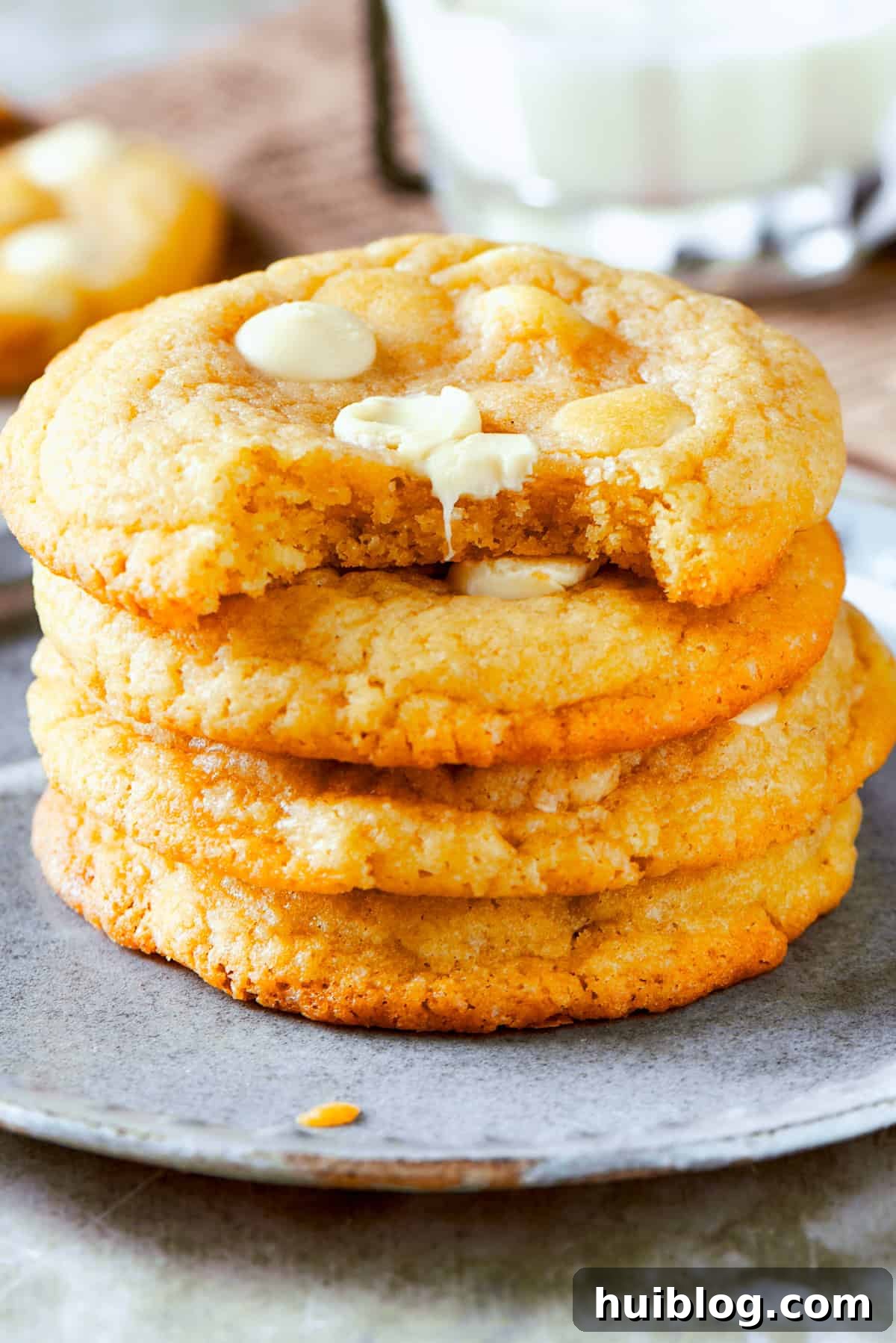 Four perfectly baked, golden-brown white chocolate chip cookies are neatly stacked on a white plate, ready to be enjoyed.