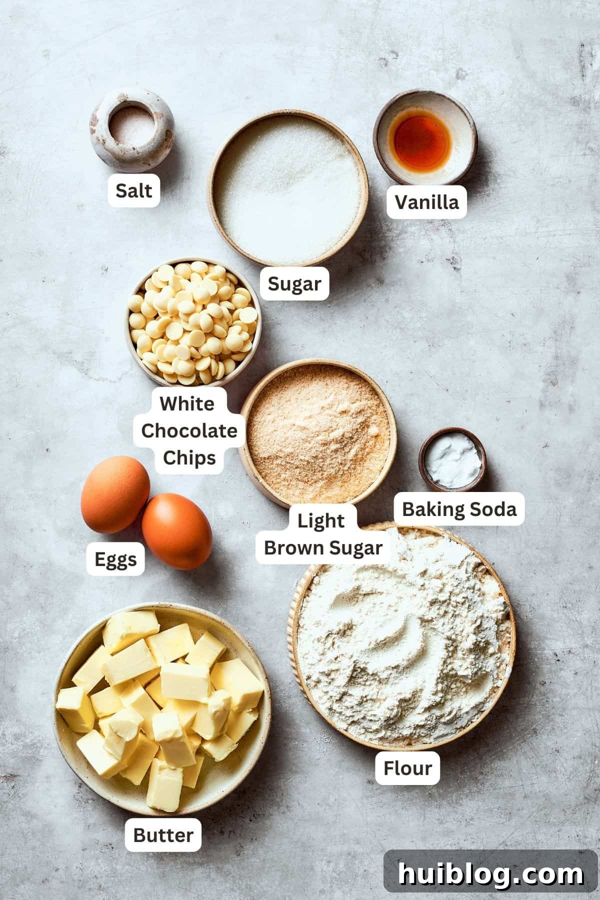All the essential ingredients for making chewy white chocolate chip cookies are neatly laid out and portioned, including white chocolate chips, all-purpose flour, butter, granulated sugar, brown sugar, baking soda, eggs, vanilla extract, and a pinch of salt.