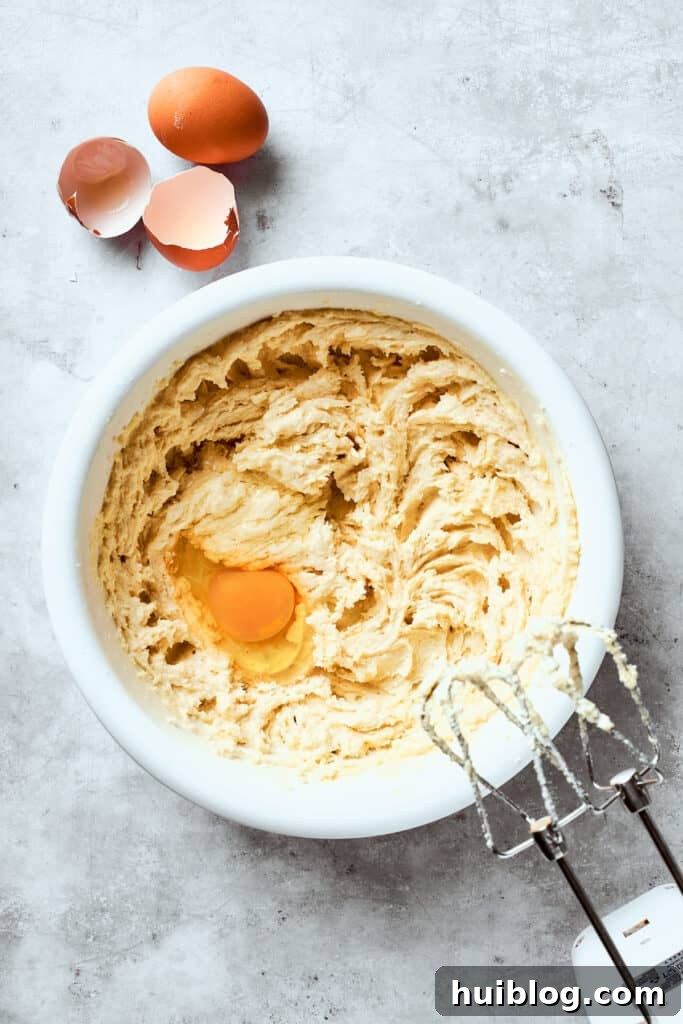 A large egg is cracked and beaten into the fluffy mixture of butter and sugars, ensuring smooth incorporation into the cookie dough.