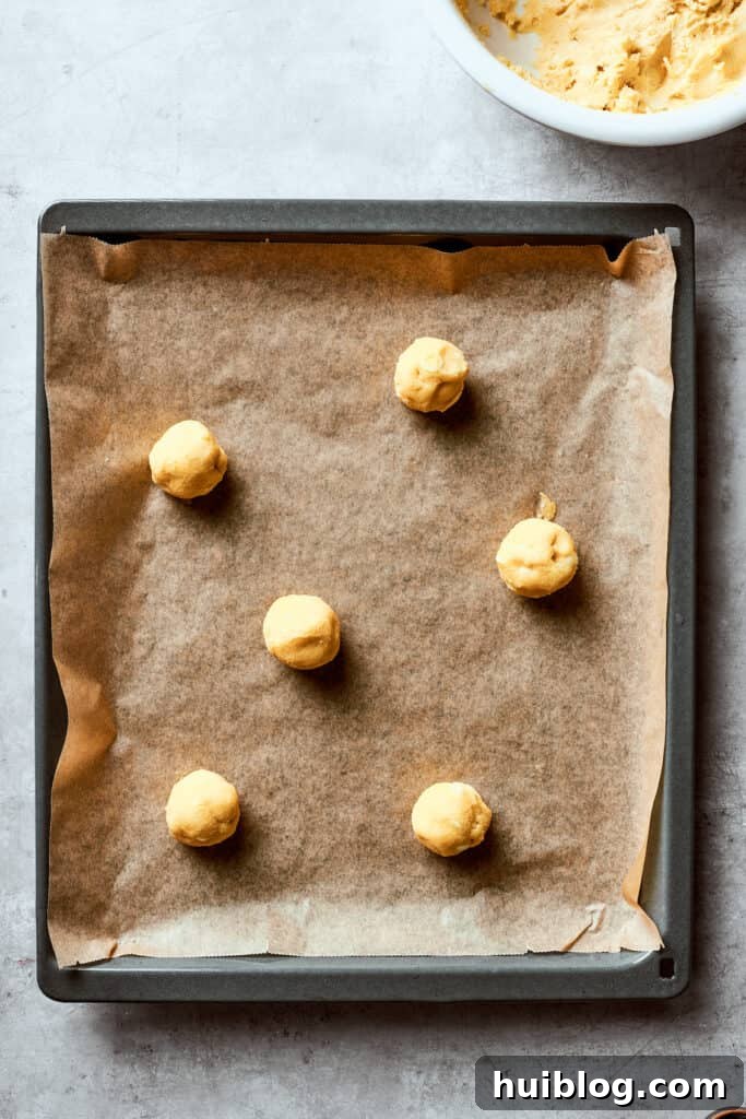 A lined baking sheet with evenly spaced balls of white chocolate chip cookie dough, ready for baking.