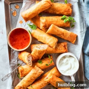 A vibrant platter showcases an array of freshly fried, golden-brown chicken egg rolls, accompanied by small bowls of bright red sweet chili sauce and creamy white dipping sauce, ready for serving.