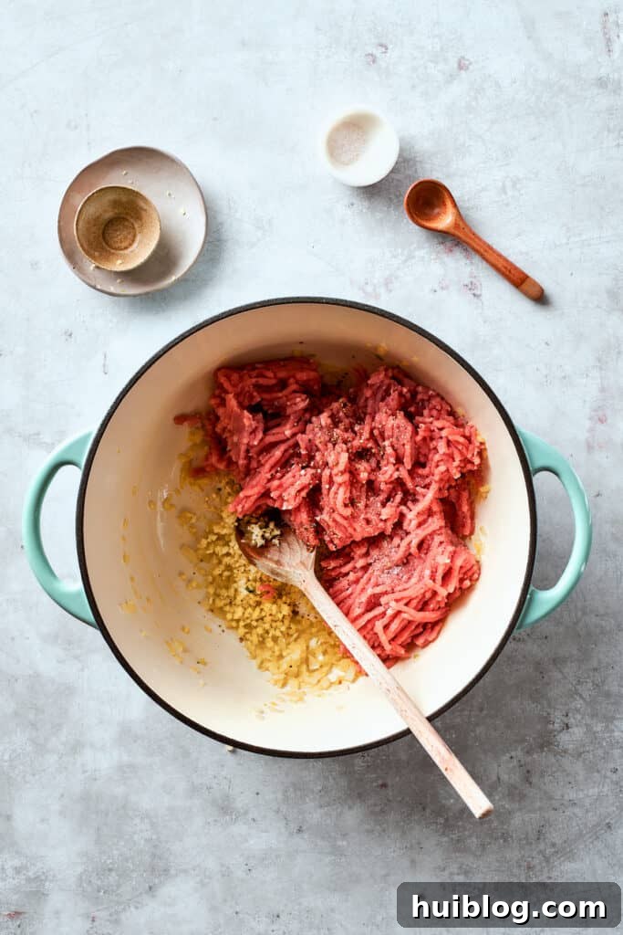 Ground chicken is added to a hot skillet, ready to be cooked and browned for the egg roll filling, alongside sautéed onions.