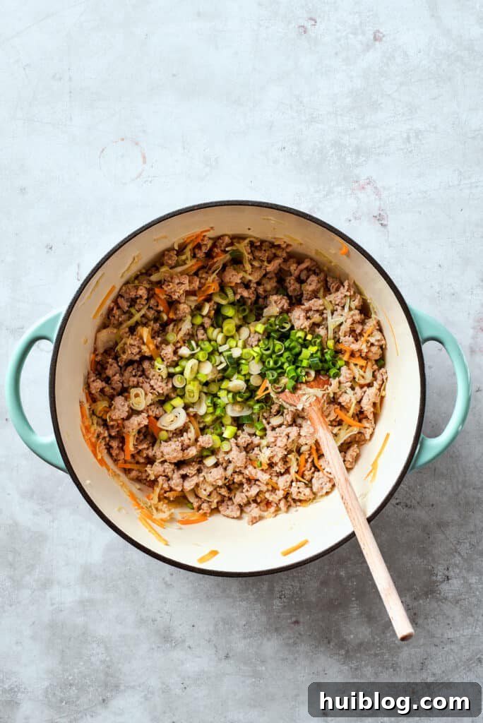 Freshly sliced green onions are being stirred into the fragrant chicken and vegetable filling in a skillet, adding a final touch of fresh flavor.