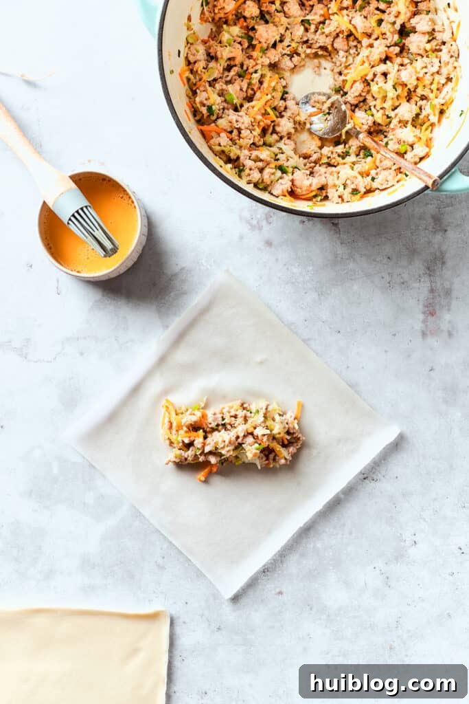 A chicken egg roll is in the process of being assembled, with a generous portion of the savory chicken and vegetable filling carefully placed in the center of a diamond-shaped egg roll wrapper.