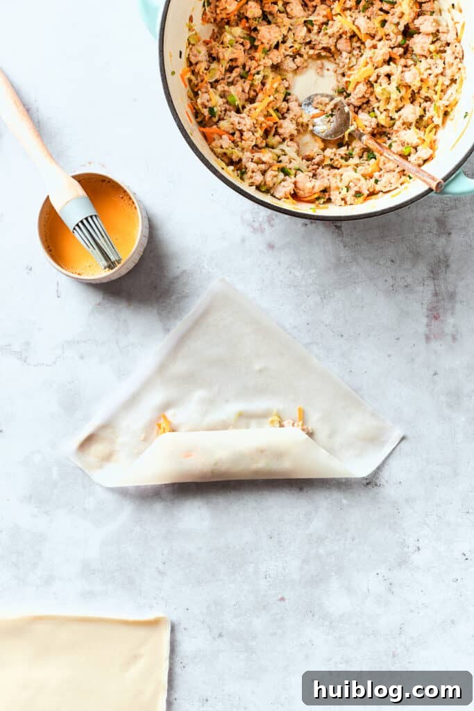 The egg roll wrapper is expertly folded around the chicken and vegetable filling, with the bottom corner folded over and the side corners brought towards the center, creating a secure package.