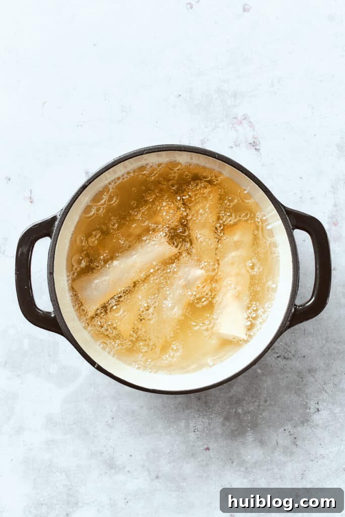 Several neatly wrapped chicken egg rolls are submerged in a pot of shimmering hot oil, frying to a perfect golden brown and developing their characteristic crispy texture.
