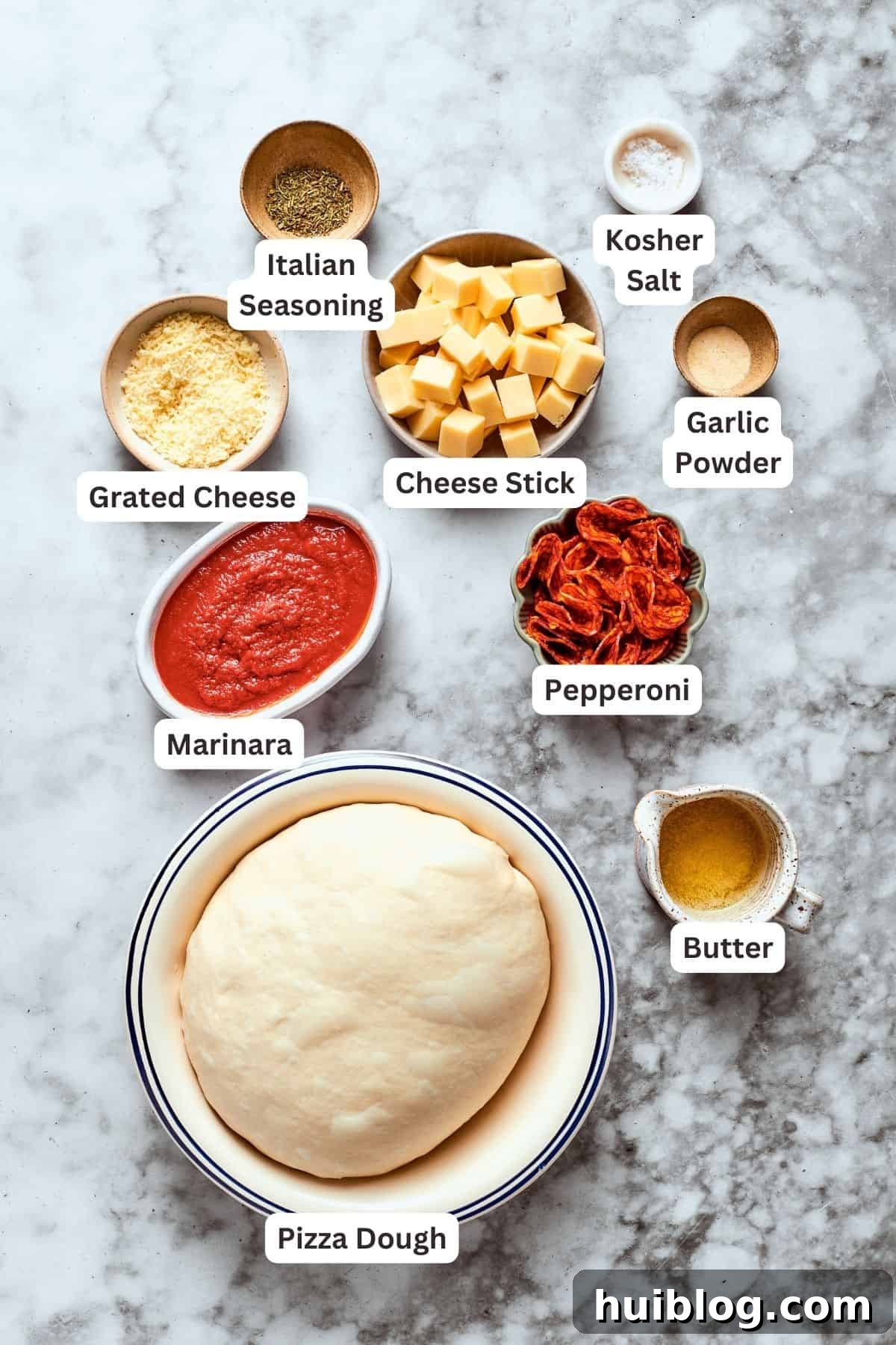 All the fresh ingredients ready for assembling delicious pizza bites. Ingredients for pizza bites are labelled and portioned out: pizza dough, grated cheese, Italian seasoning, marinara sauce, pepperoni, butter, garlic powder, cheese stick, salt.
