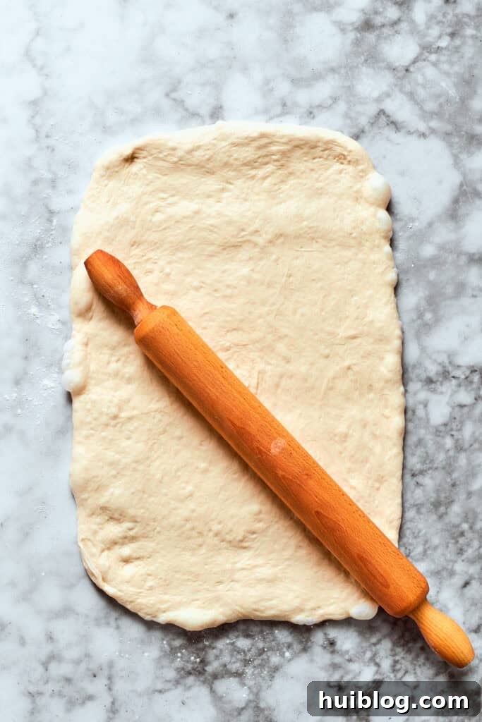 Rolling out the pizza dough to an even thickness. The pizza dough is rolled out with a rolling pin into a rectangular shape.