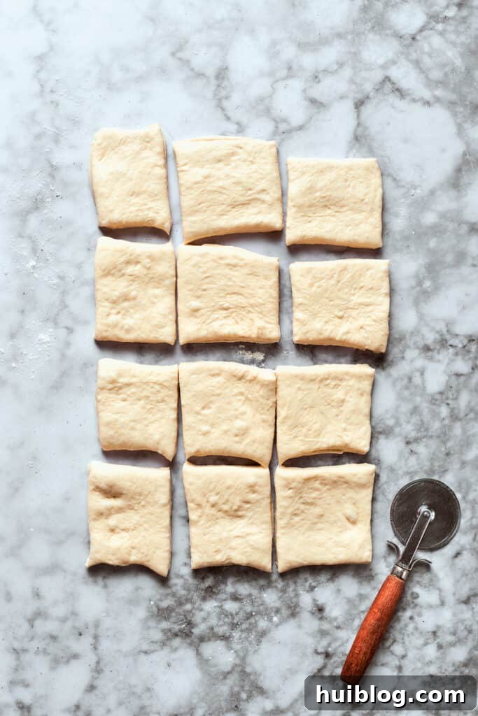 Dividing the dough into perfect squares for uniform bites. The rolled out pizza dough is cut into 12 even squares using a sharp knife.