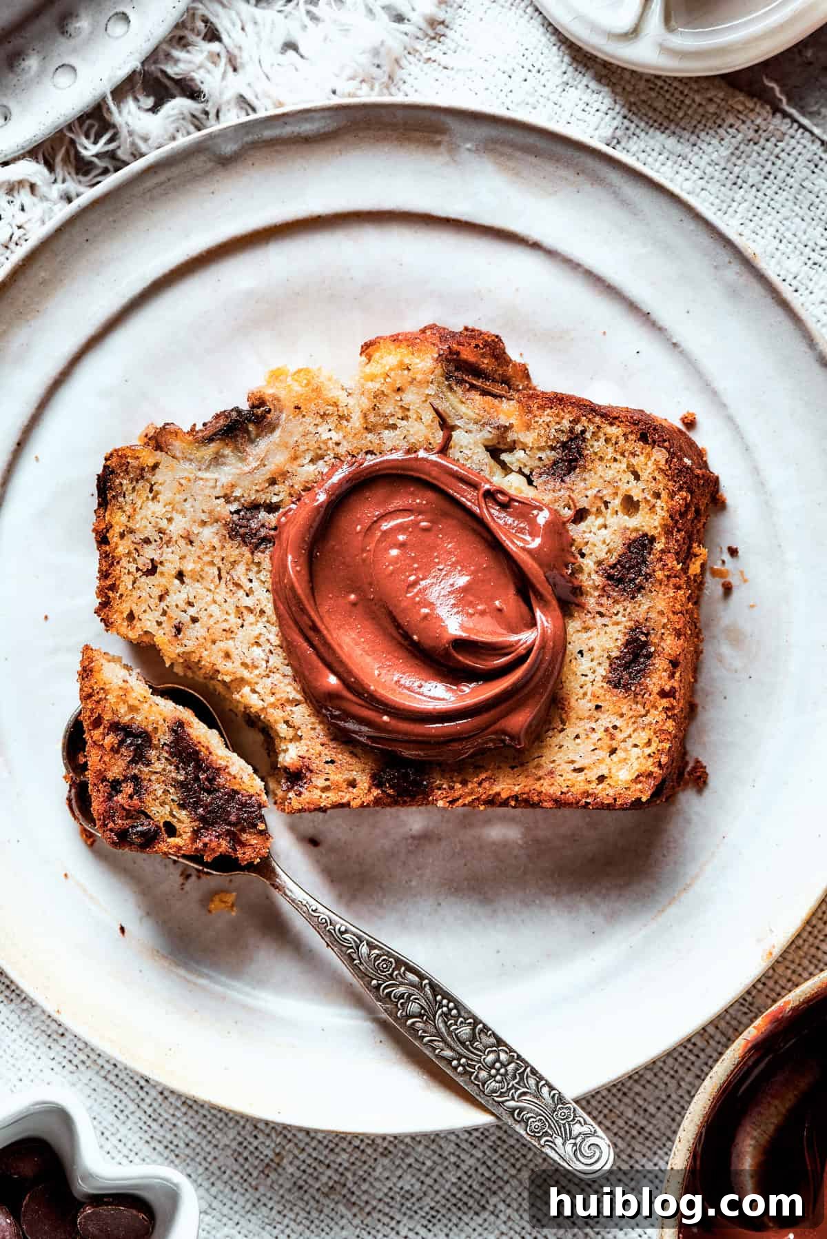 A hand spreading rich Nutella over a slice of moist sour cream banana bread, creating a decadent breakfast or snack.