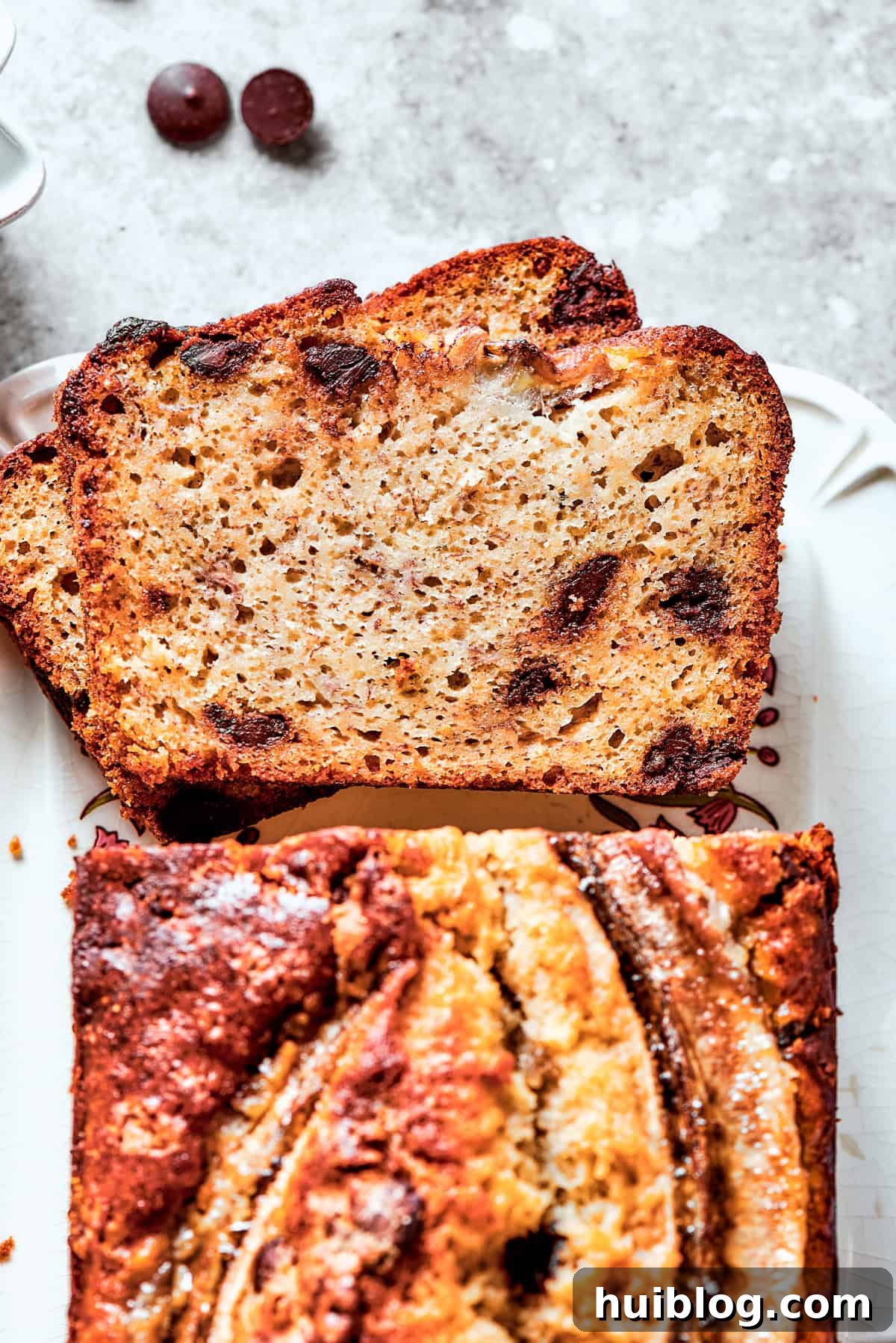 An overhead shot showcasing a baked sour cream banana bread loaf, with two slices cut out to reveal its incredibly moist interior dotted with chocolate chips.