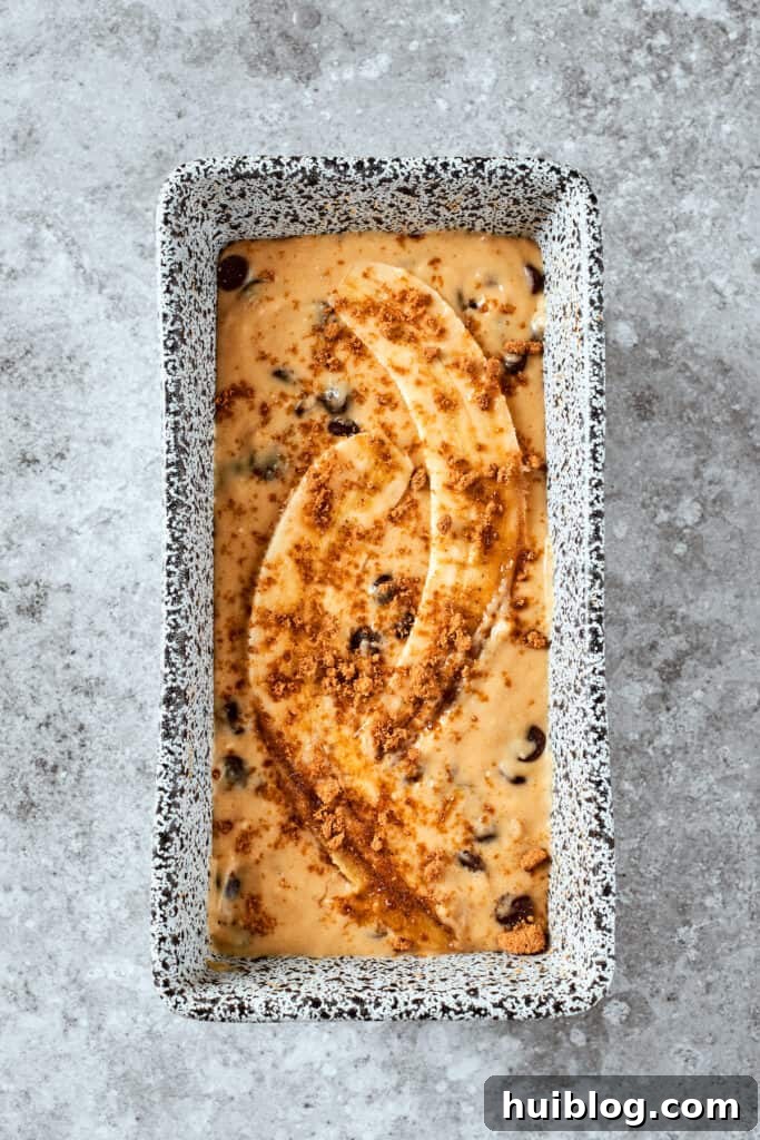 The rich banana bread batter is poured into a prepared loaf pan and artfully topped with sliced banana halves, ready for baking.