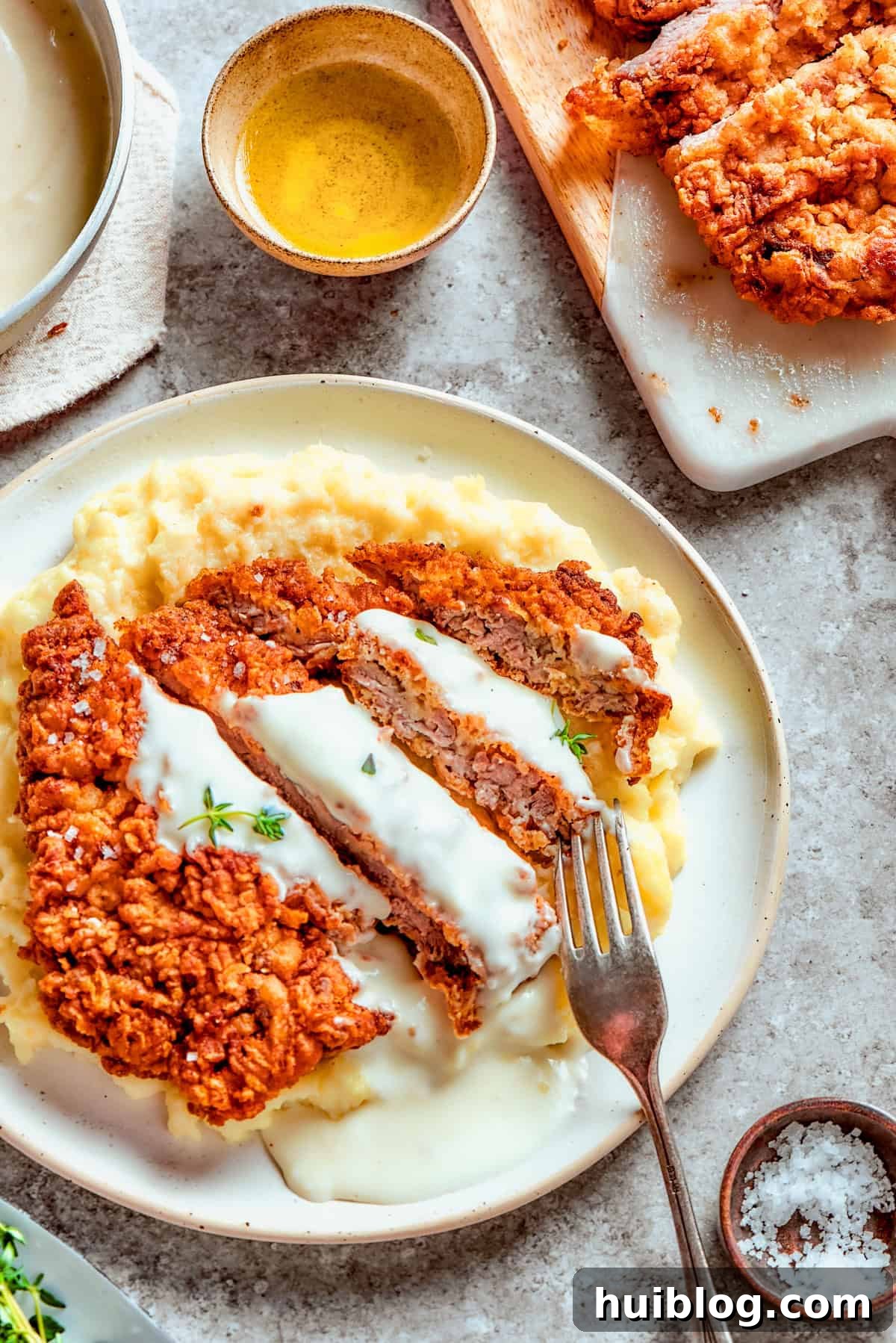 Sliced chicken fried steak served over mashed potatoes, and a fork is resting on top of the meat.