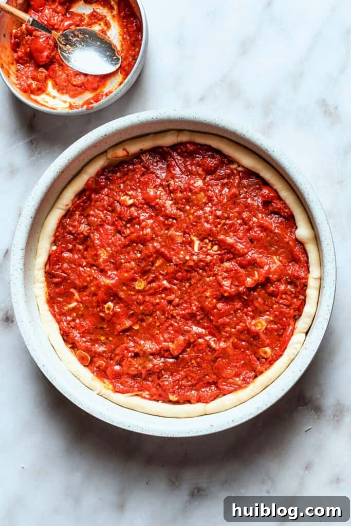 The thick tomato sauce is generously added over the cheese layer on the deep dish pizza, ensuring every bite is flavorful.