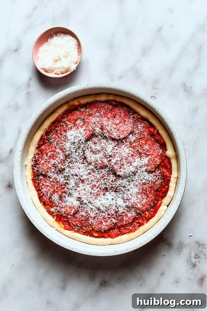 Freshly grated Parmesan cheese is scattered over the top of the deep dish pizza, adding a final savory touch.