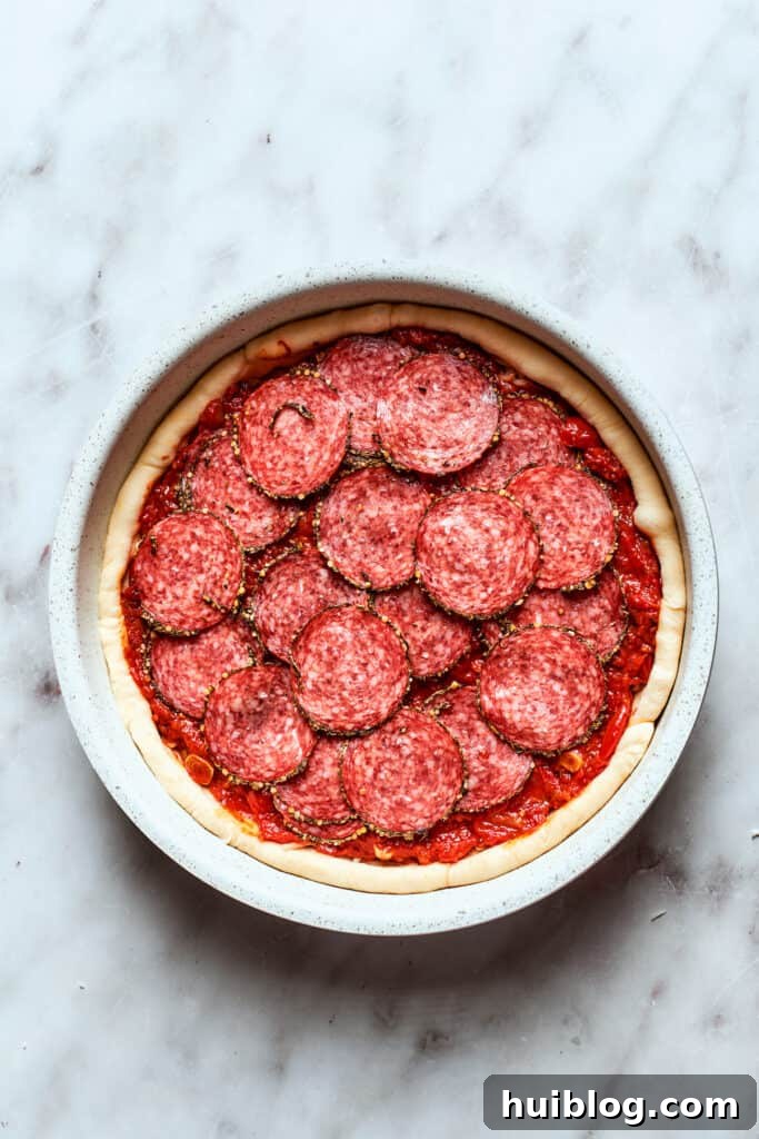 The assembled deep dish pizza, topped with all its glorious ingredients, is ready to be baked to perfection.