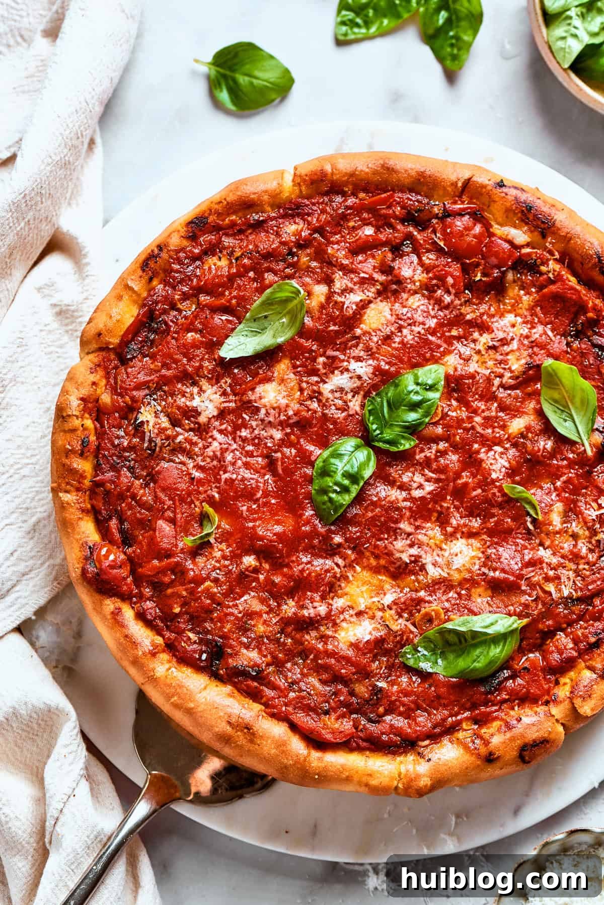 Another overhead image of the deep dish pizza, showcasing its golden crust, thick sauce, and bubbling cheese, garnished with fresh basil for a vibrant touch.