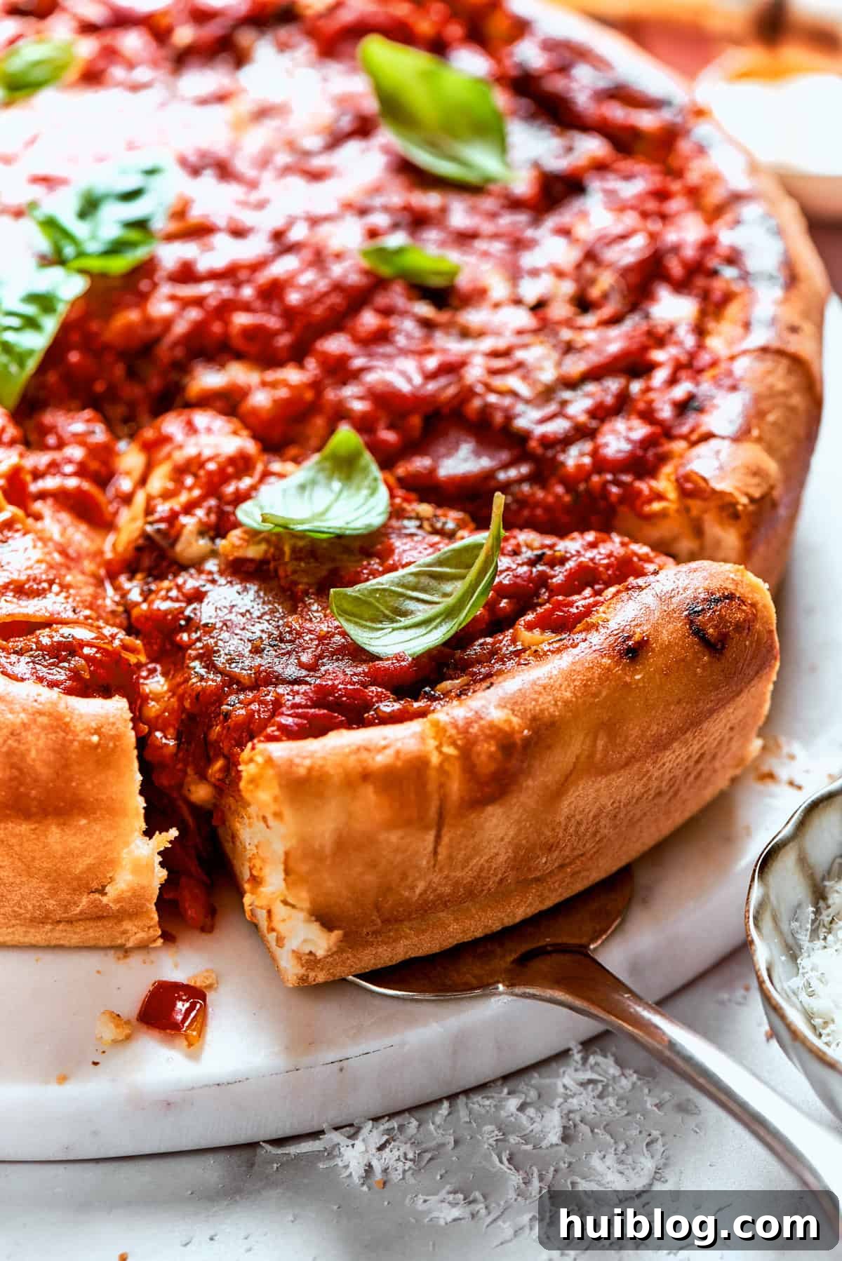 A serving spoon carefully lifts a perfect slice of deep dish pizza out of the pan, revealing its distinct layers of cheese, sauce, and crust.