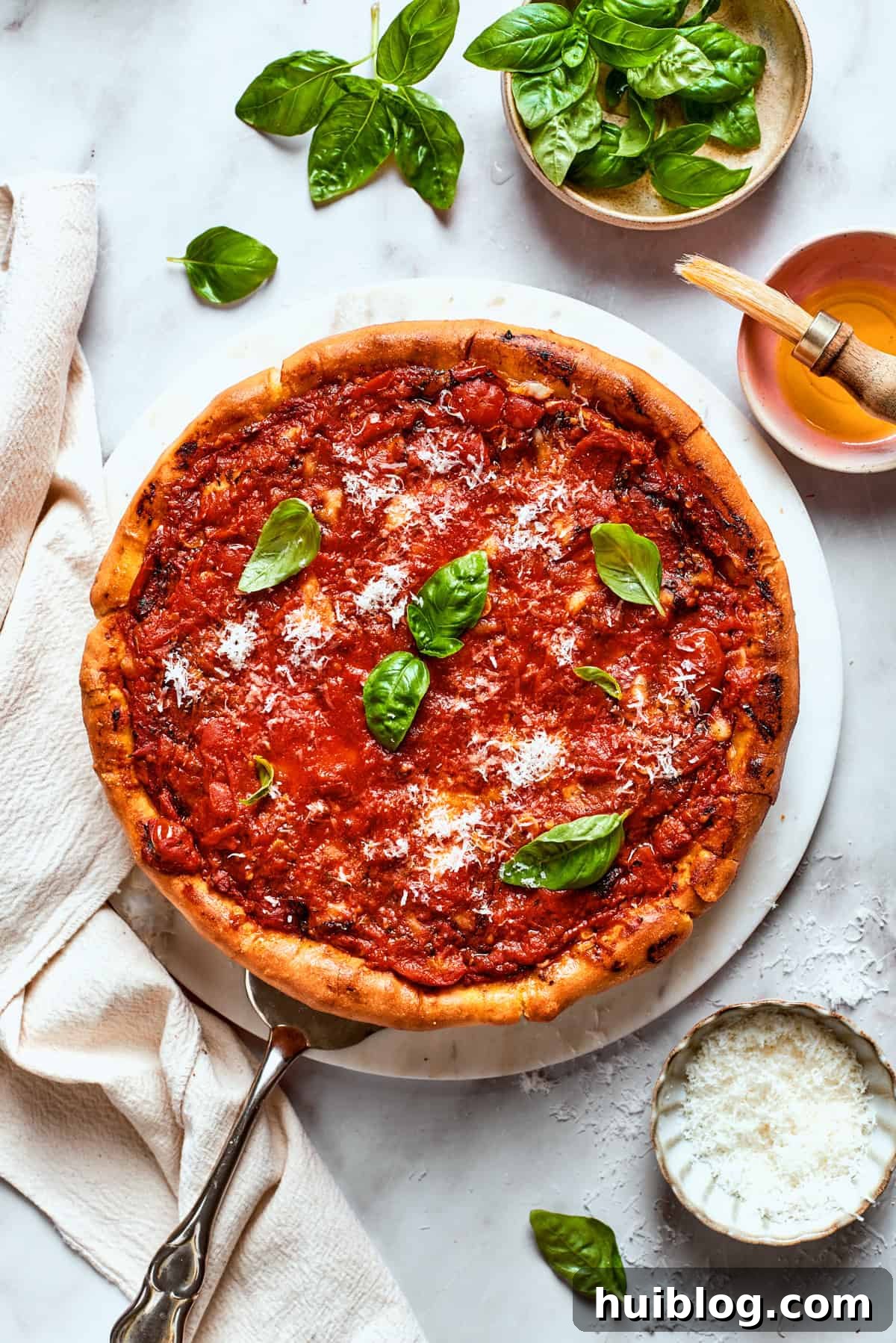 Overhead image of a baked deep dish pizza, garnished with vibrant fresh basil leaves, ready to be sliced and served.