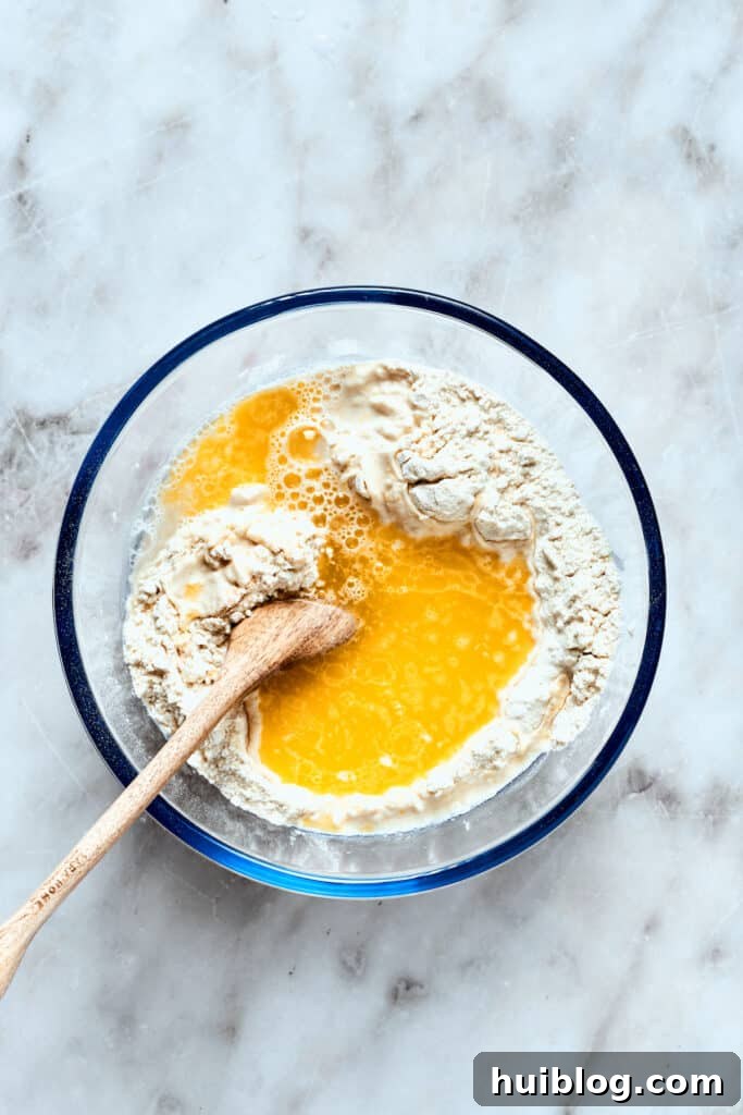 Warm water and melted olive oil are being poured into the bowl of dry ingredients for the pizza dough, ready to be mixed.