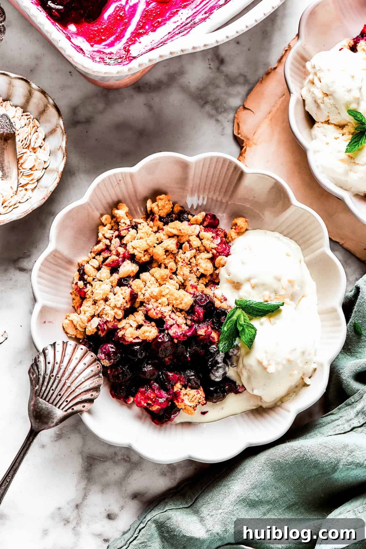 Bursting with juicy berries, this Blueberry Crisp Recipe is topped with a buttery brown sugar and oat crumble. Blueberry crisp served in a bowl with two scoops of vanilla ice cream and a garnish of mint.