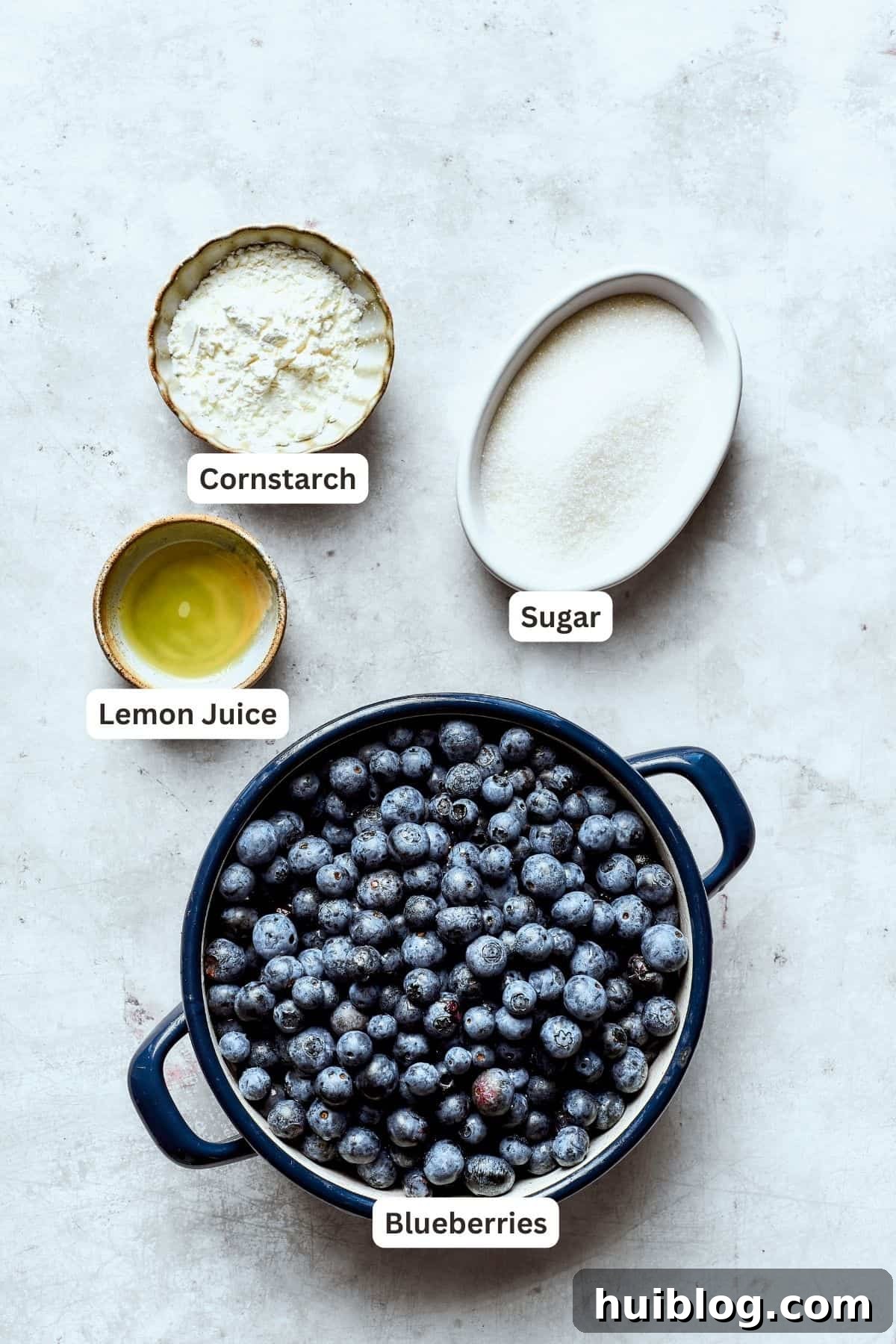 Bursting with juicy berries, this Blueberry Crisp Recipe is topped with a buttery brown sugar and oat crumble. Ingredients for blueberry crisp filling are labeled and portioned: cornstarch, sugar, blueberries, lemon juice.