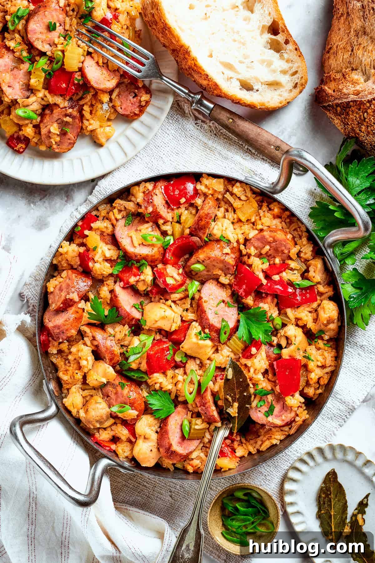 A large, rustic pan filled with a hearty serving of Chicken and Sausage Jambalaya, placed on a wooden table alongside crusty bread and a serving utensil, inviting guests to share.