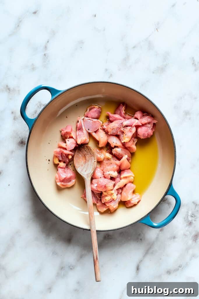 Bite-sized pieces of chicken being seared in olive oil within a large pot, achieving a golden-brown crust.