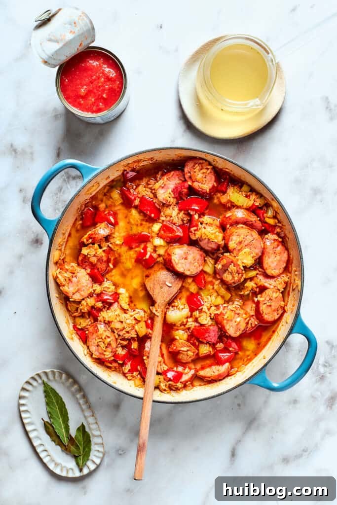 A wooden spoon thoroughly stirring all the ingredients together in the pot, combining the chicken, sausage, vegetables, rice, and spices before liquid is added.